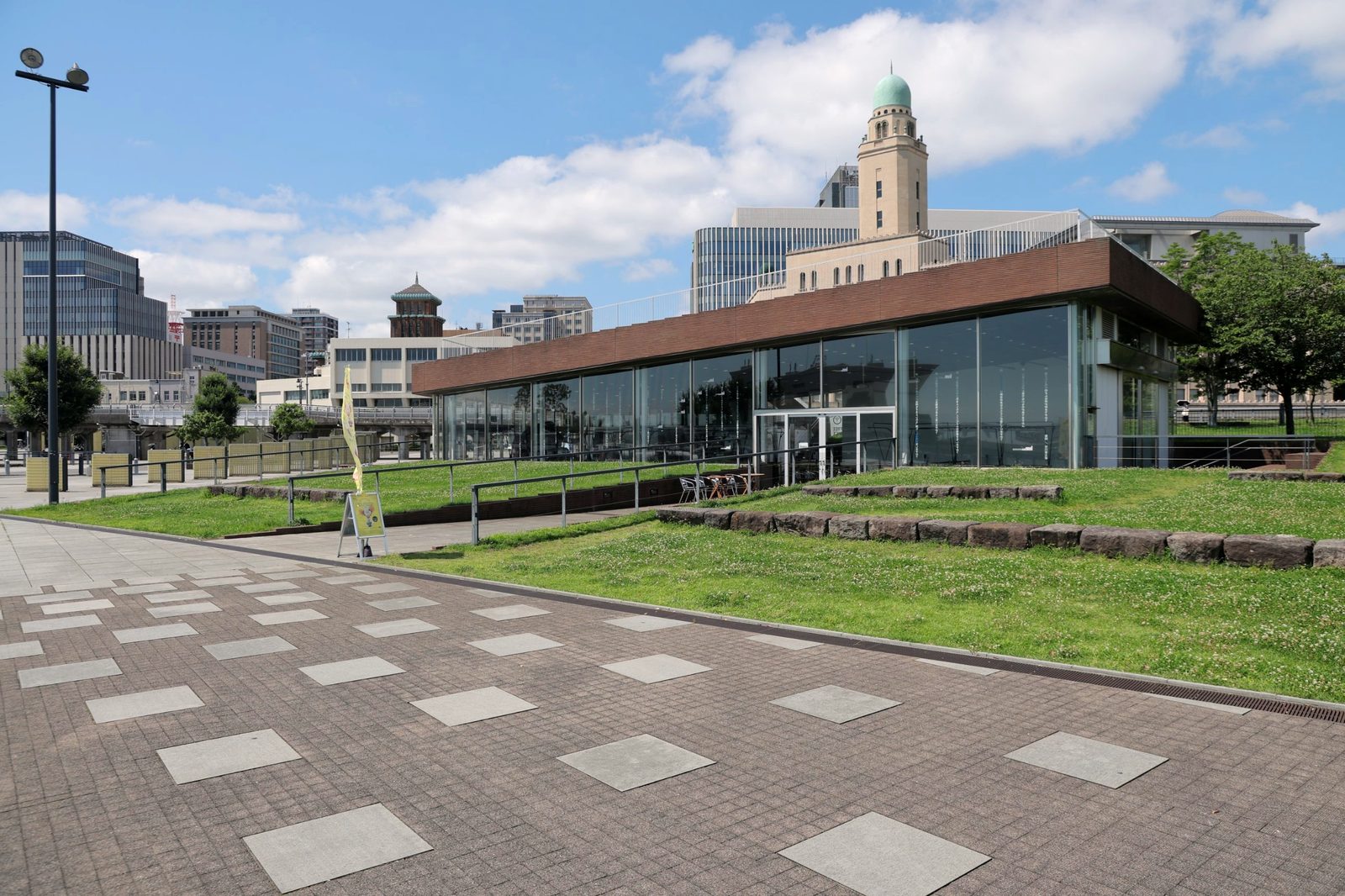 象の鼻テラスの外観。芝生の丘に建つガラス張りの建物と、背後の横浜税関と神奈川県庁の塔